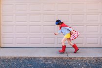 Chica corriendo más allá de una puerta de garaje vestido como un superhéroe - foto de stock