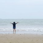Menina de pé na praia junto ao oceano com os braços estendidos, Zhoushan, China — Fotografia de Stock