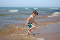 Niño en la playa corriendo fuera del mar, Corfú, Grecia - foto de stock