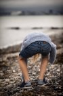 Мальчик, стоящий на пляже и собирающий ракушки — стоковое фото