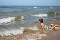 Niño acostado en el oleaje en la playa, Corfú, Grecia - foto de stock