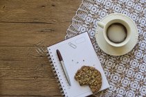 Taza de café con una galleta en una mesa con bloc de notas y bolígrafo - foto de stock