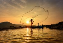 Silhouette di un pescatore che getta la rete da pesca in un fiume, Thailandia — Foto stock