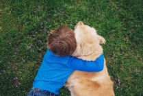 Overhead view of a boy hugging his golden retriever dog — Stock Photo