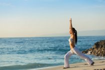 Eine junge Asiatin macht Yoga an einem weißen Sandstrand auf Bali. Sie trägt eine lange weiße Hose und ein Bikini-Oberteil. — Stockfoto