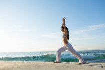 Una giovane donna asiatica sta facendo yoga in una spiaggia di sabbia bianca a Bali. Lei indossa lunghi pantaloni bianchi e un top bikini. — Foto stock