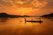 Pescador de silluato e barco no rio durante o pôr do sol, pescador trowing as redes sobre durante o pôr do sol, durante o pôr do sol, Tailândia — Fotografia de Stock