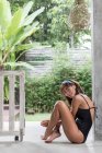 A young caucasian woman in a black swimsuit is enjoying the pool environment in her tropical balinese villa. — Fotografia de Stock