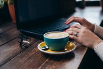 Cup of coffee next to a woman using laptop — Stock Photo