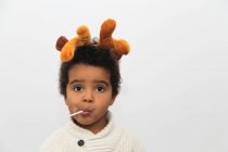 Retrato de un niño sonriente con cuernos de Navidad comiendo una piruleta - foto de stock