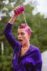 Жінка з рожевим волоссям наливає склянку води над головою — стокове фото