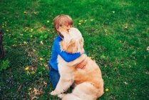 Jeune garçon jouant avec le chien golden retriever dehors dans l'herbe — Photo de stock