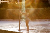 Chica de pie bajo una ducha pública en un parque - foto de stock