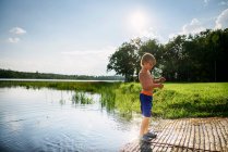Jeune garçon pêche dans un lac paisible avec reflet du ciel et des nuages — Photo de stock