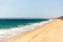 Praia de areia com ondas e céu azul — Fotografia de Stock