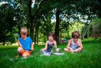 Drei kleine Kinder sitzen im Hinterhof und lesen Bücher und essen frisches Gemüse — Stockfoto