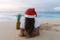 Mujer con un sombrero de Papá Noel de Navidad tirado en la playa junto a una piña, Haleiwa, Hawai, América, EE.UU. - foto de stock