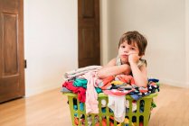 Boy sitting on floor leaning on a laundry basked filled with clothes — Stock Photo