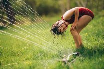 Young girl playing in a sprinkler in the backyard — Stock Photo