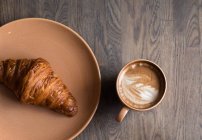 Xícara de café e croissant na mesa de madeira — Fotografia de Stock