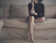 Giovane donna seduta sul divano, colpo ritagliato — Foto stock