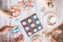 Top view of hands with colorful macarons on wooden table — Stock Photo