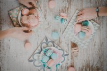 Vue de dessus des mains avec des macarons colorés sur table en bois — Photo de stock