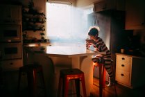 Niño sentado en la cocina comiendo su desayuno en la luz de la mañana - foto de stock