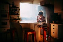 Garçon assis dans la cuisine manger son petit déjeuner dans la lumière du matin — Photo de stock