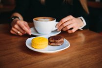 Woman enjoying a cup of coffee and macaroons — Stock Photo