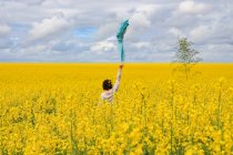 Женщина, стоящая в поле рапса, размахивая шарфом в воздухе, Ньор, Нувель-Аквитания, Франция — стоковое фото