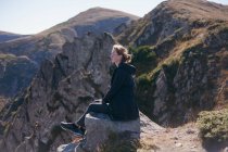 Mujer sentada en un acantilado mirando a la vista de la montaña, Ucrania - foto de stock