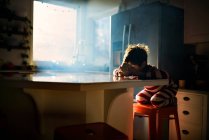 Niño sentado en la cocina comiendo su desayuno en la luz de la mañana - foto de stock