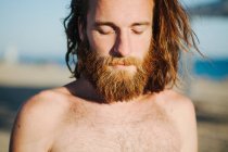 Portrait of a man with long hair and a beard standing on beach — Stock Photo