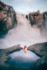 Vue arrière d'une femme dans une piscine rocheuse regardant la cascade d'Aldeyjarfoss, Highlands, Islande — Photo de stock