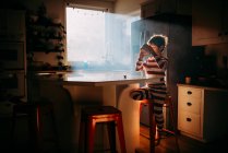 Хлопчик стоїть на кухні їсть свій сніданок у ранковому світлі — стокове фото