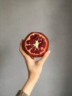 Woman hand holding a pomegranate against grey wall — Stock Photo