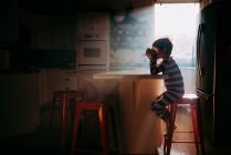 Мальчик, сидящий на кухне и завтракающий в утреннем свете — стоковое фото