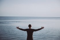 Чоловік стоїть біля океану з простягнутими руками — стокове фото