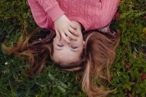 Девушка лежит на траве, закрывая рот рукой. — стоковое фото