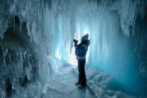 Donna in piedi in una grotta di ghiaccio che scatta una foto, Oblast 'di Irkutsk, Siberia, Russia — Foto stock