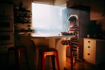 Хлопчик стоїть на кухні їсть свій сніданок в ранковому світлі — стокове фото