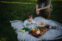 Мальчик сидит на одеяле для пикника и ест рядом с отцом. — стоковое фото