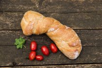 Loaf of bread and cherry tomatoes on a wooden table — Stock Photo