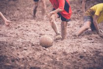 Deux garçons jouant au football dans la boue avec leurs amis — Photo de stock