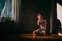 Girl sitting on the floor in her pyjamas holding her hands in front of her face — Stock Photo