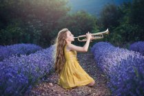 Девушка, сидящая на лавандовом поле и играющая на трубе — стоковое фото