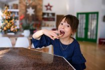 Chica de pie en una cocina comiendo una galleta de Navidad - foto de stock