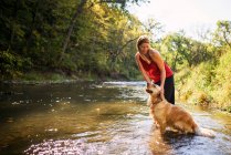 Femme debout dans une rivière avec un chien golden retriever — Photo de stock