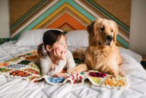 Giovane ragazza che gioca con il cane su un letto — Foto stock